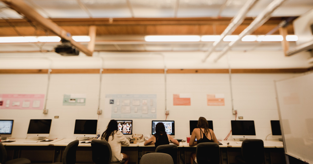 three students work on computers in an airy classroom