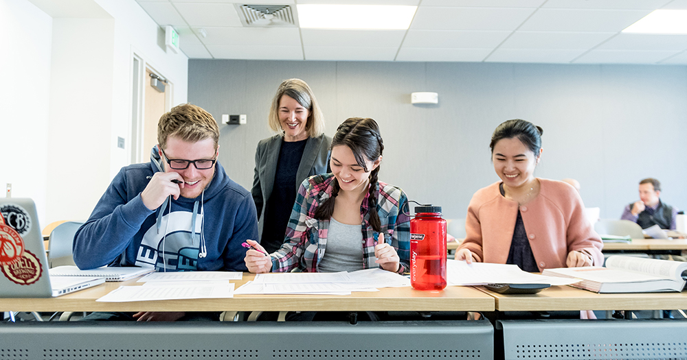 Three students work at table with teacher nearby