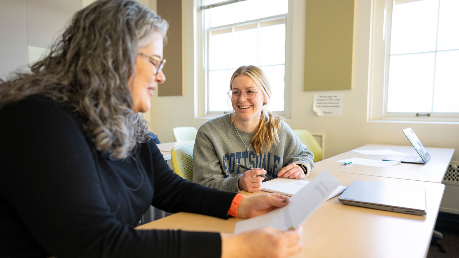 A student and an economics professor have a discussion over papers and a laptop