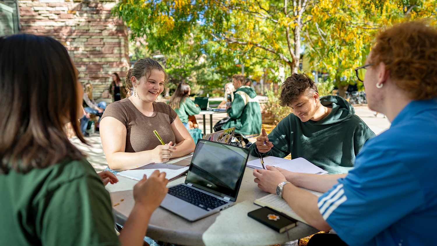 Students discuss classes under trees at an outdoor table