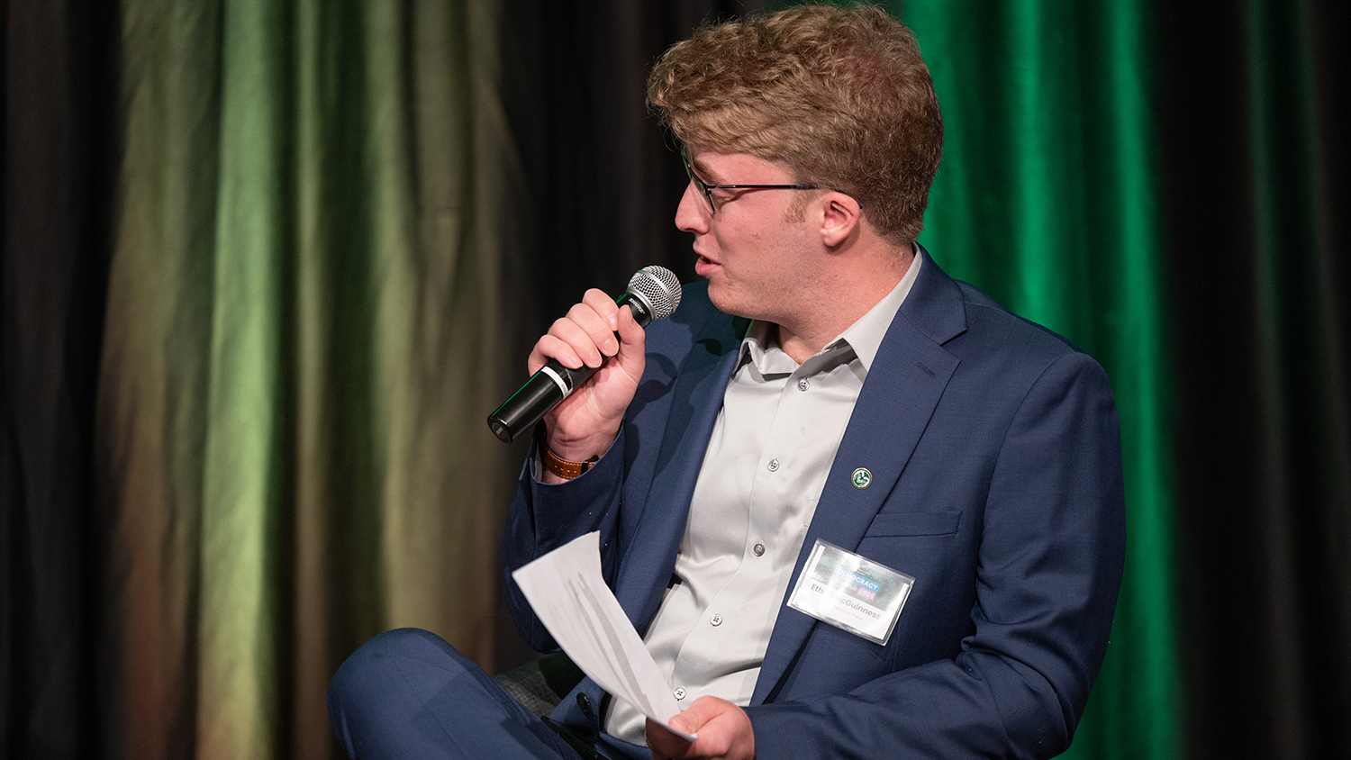 A student speaks into a mic on stage at a political event