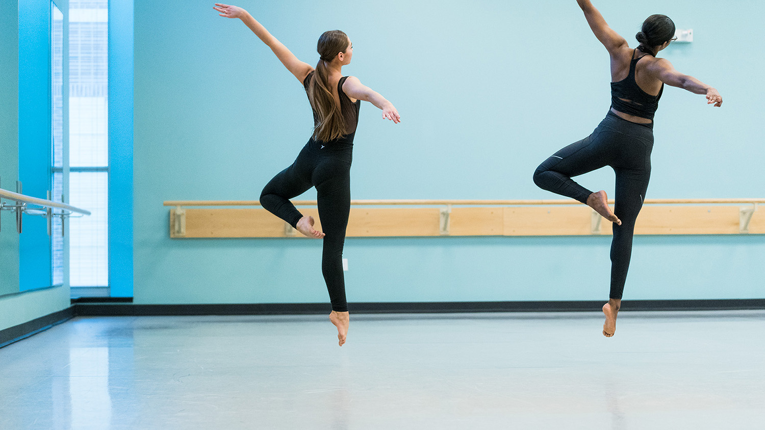Two CSU dancers are captured mid-leap in the rehearsal studio