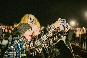 A creepy clown poses for a photo with students at a corn maze