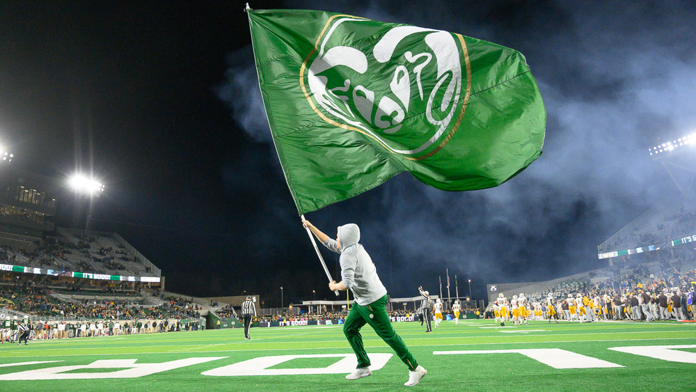 CSU student running across football field with giant CSU flag