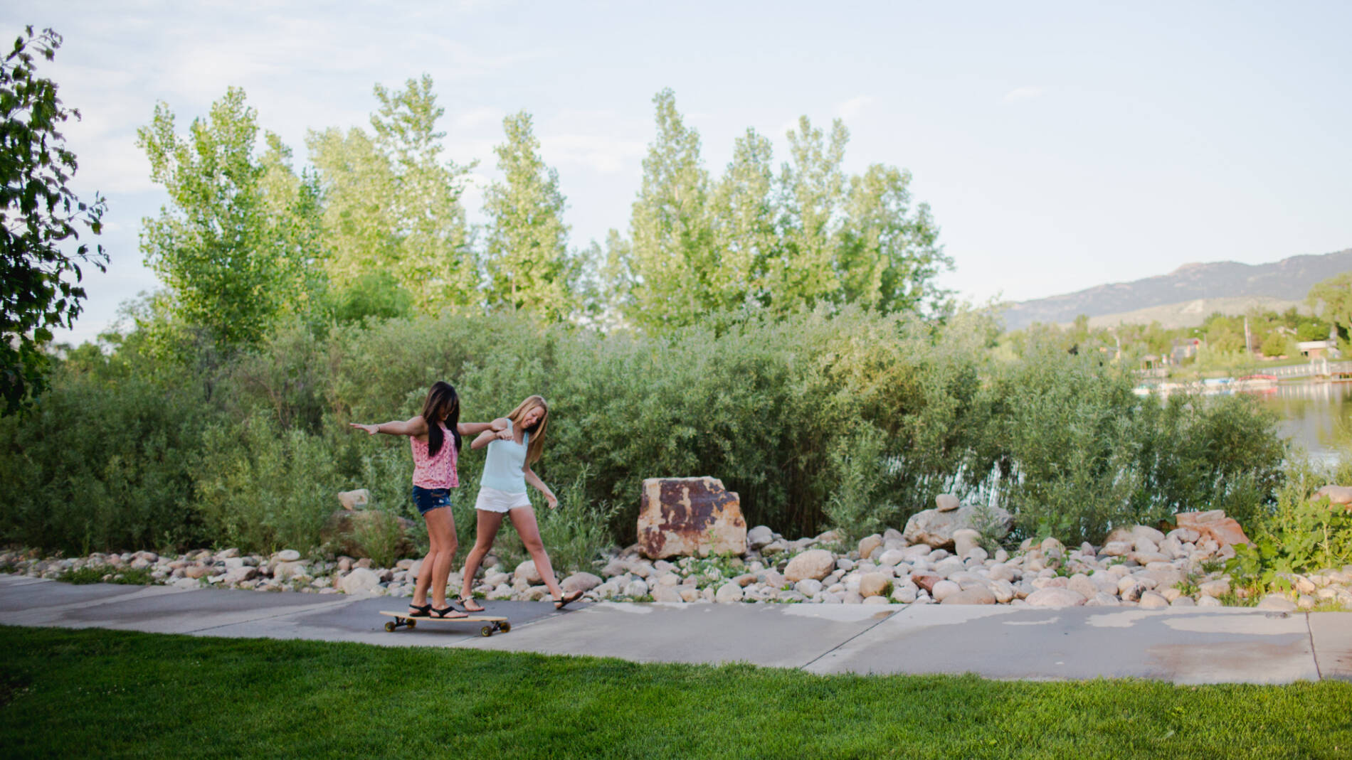 One woman steadies another woman on a skateboard outside city park