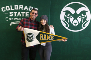Student and her dad hold a Rams pennant in front of CSU sign