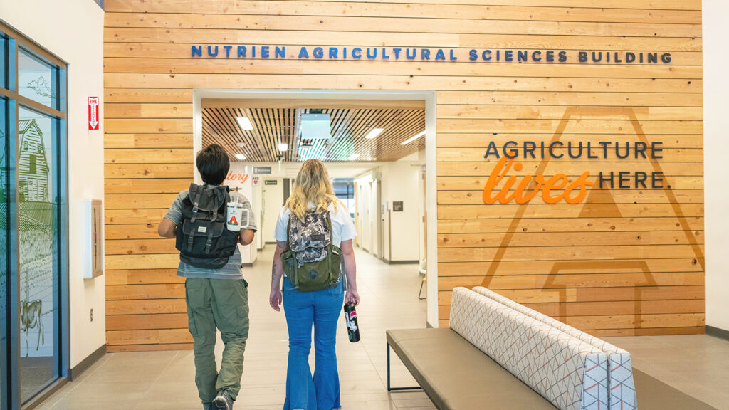 Student head toward the Nutrien Well classroom; a wall ahead of them has stylized script that says "Agriculture Lives here"