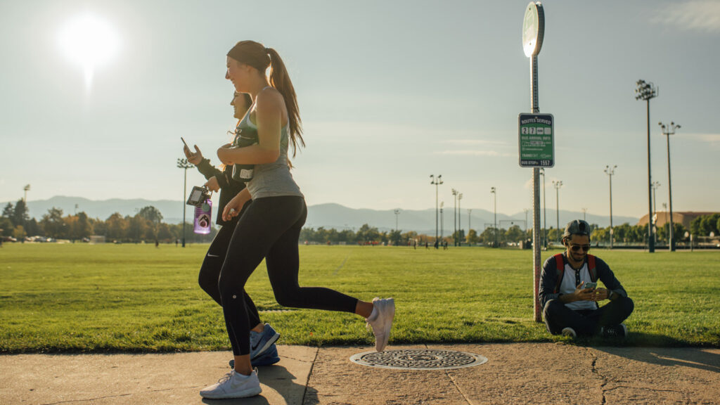 Two women running on sidewalk past person waiting for the bus