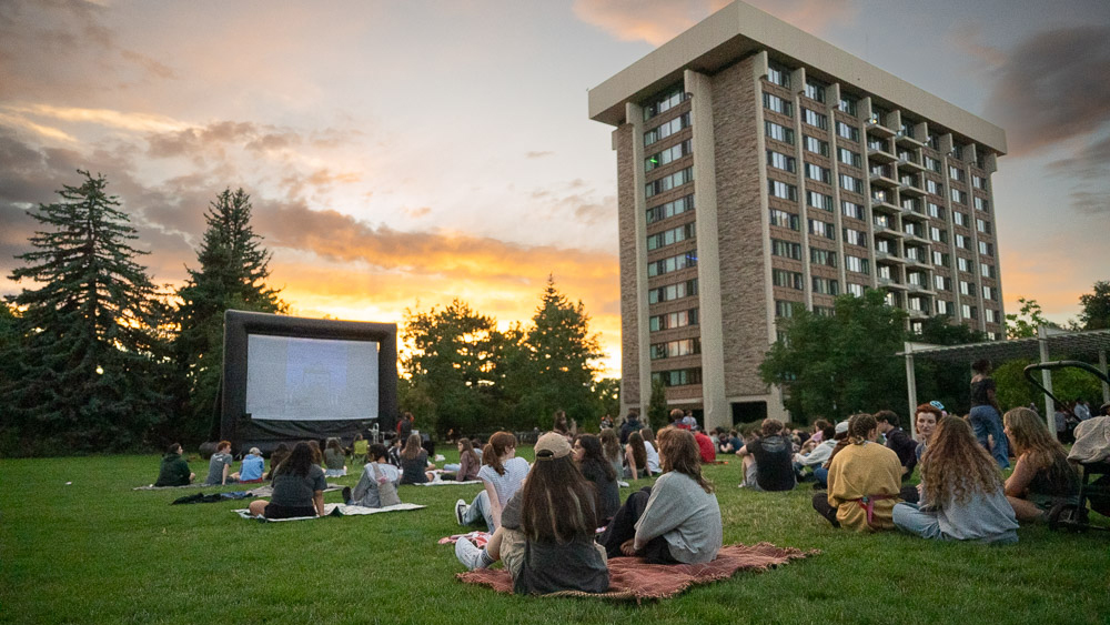 Students watch a movie on a projector screen outside a residence hall
