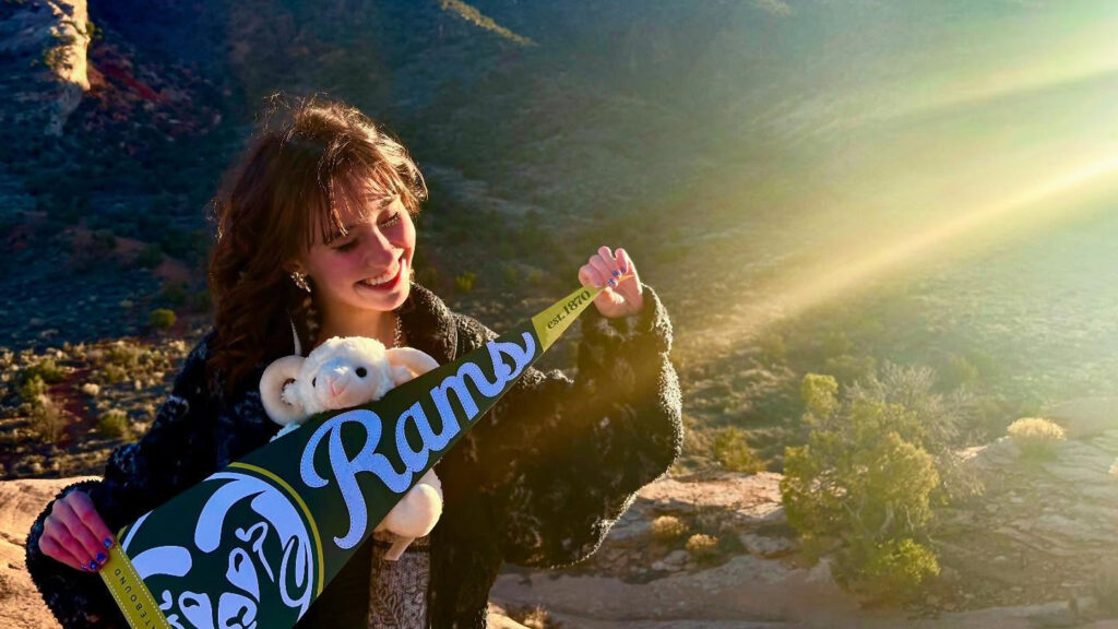 Student holding Rams banner and a stuffed Ram outside with streaks of sunlight in foreground