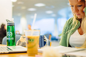 A student focuses on paperwork and a laptop with a coffee nearby