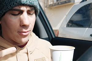Vlogger drinks coffee in car.