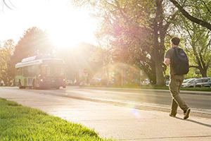 A student walks along a CSU pathway with a bus passing by