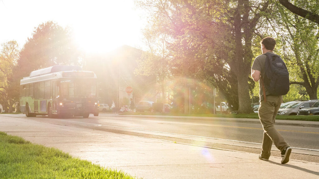 A student walks along a CSU pathway with a bus passing by