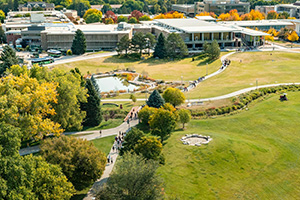Students walk on winding sidewalk among fall-colored trees and a pond on CSU campus