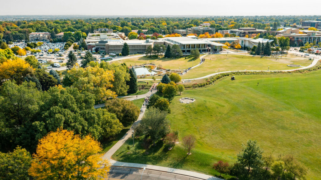 Students walk on winding sidewalk among fall-colored trees and a pond on CSU campus
