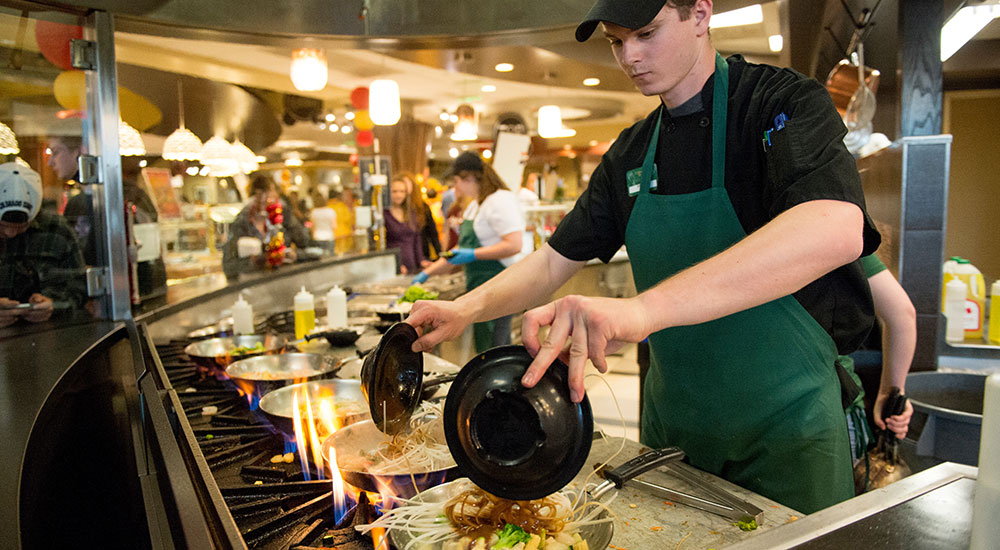 A CSU dining employee piles a bowl of fresh ingredients onto a pan.