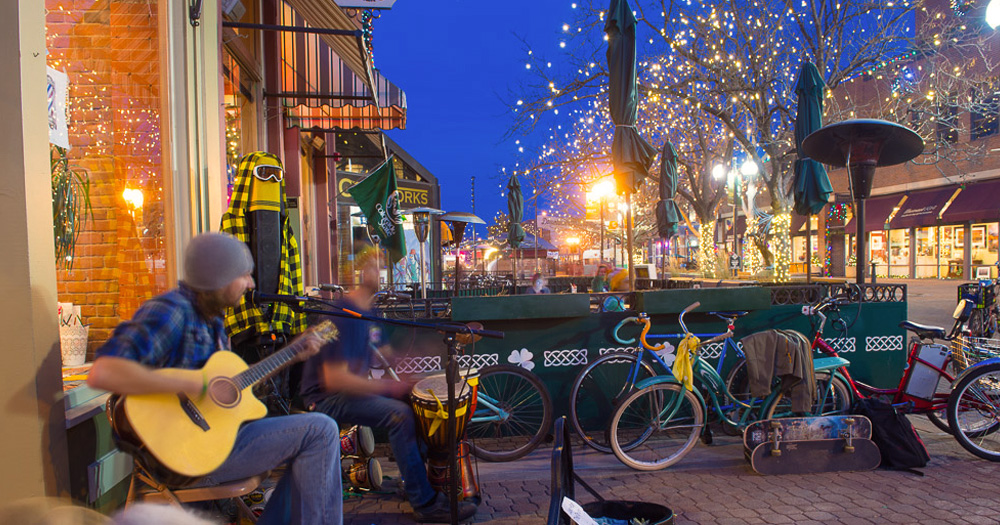 downtown fort collins at night with lights, bikes, and guy playing guitar