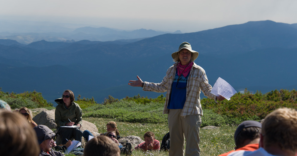 a teacher instructs to a class on the top of a mountain
