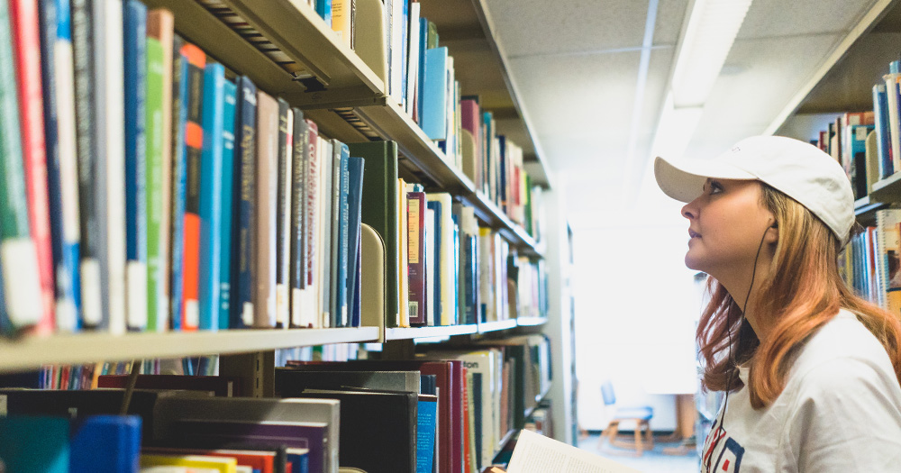 A student looks at books on a library shelf.