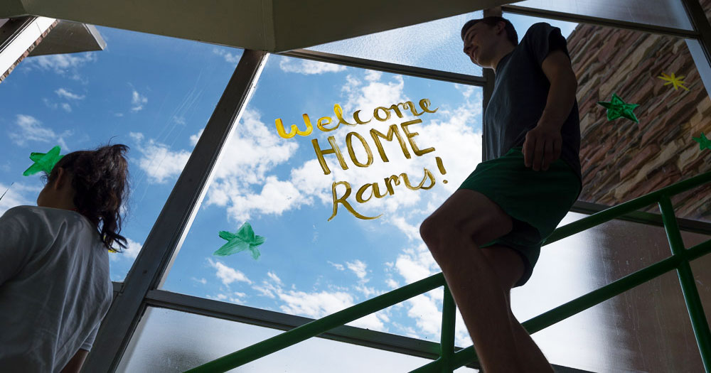 People walk down stairs next to a window with "Welcome Home Rams" painted on it.
