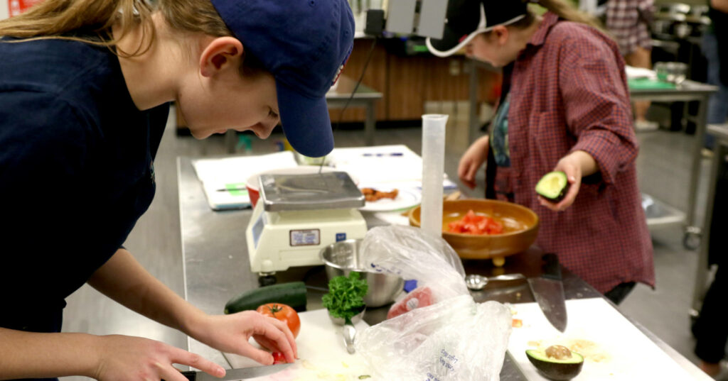 STudents work in the learning kitchn with fresh ingredients and books that help them determine nutrients.