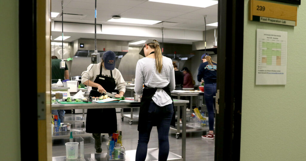 Two students work in a learning kitchen. Photo angle is from the doorway of the lab.