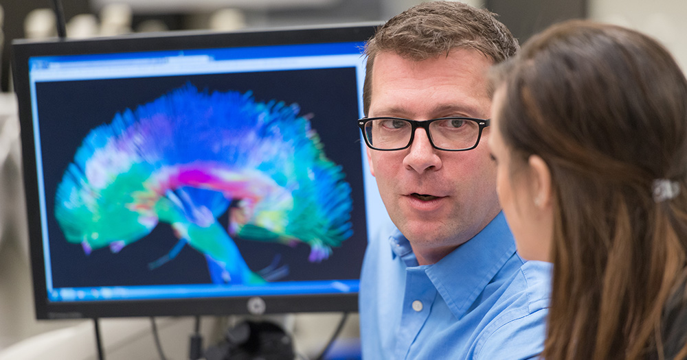 a neuroscience student works with a professor near a brain scanner