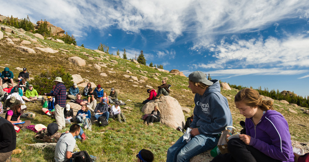 CSU students take notes while attendign class atop a mountain slope with boulders all around