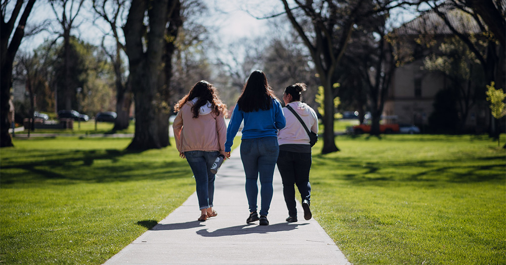 Three people walking down sidewalk on campus