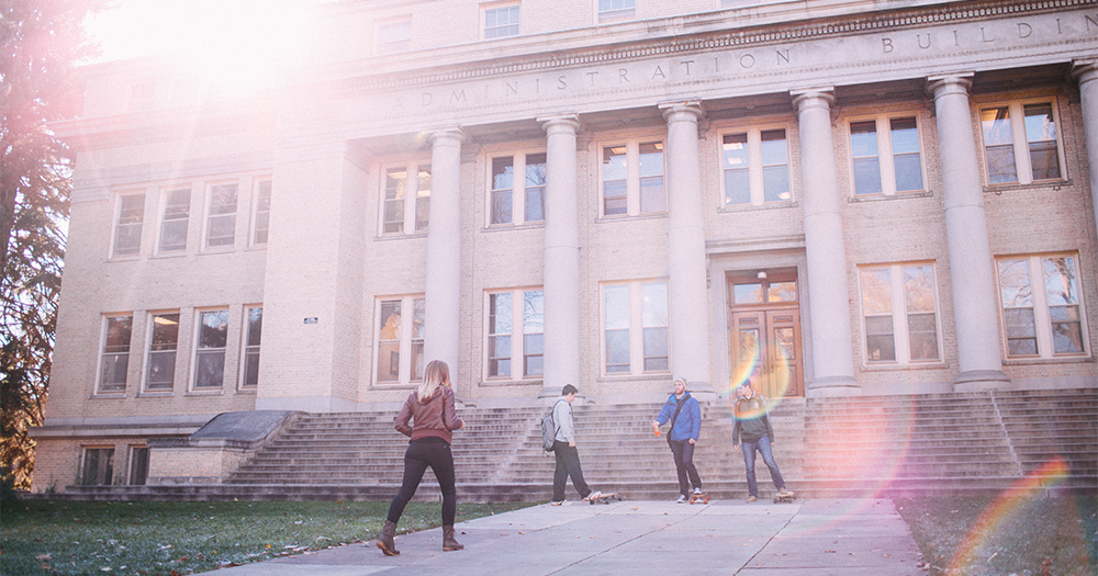 Four students gather in front of the Administration Building at Colorado State as the sun shines down onto campus.