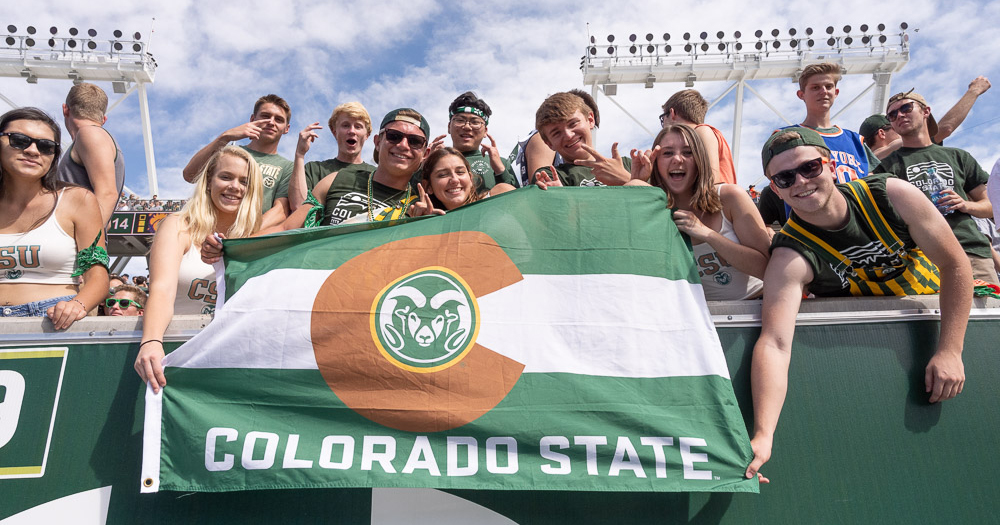 A group of smiling football fans cheer on the Colorado State Rams at Canvas Stadium.