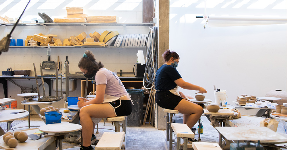 two colorado state pottery students throw pots at wheels in class