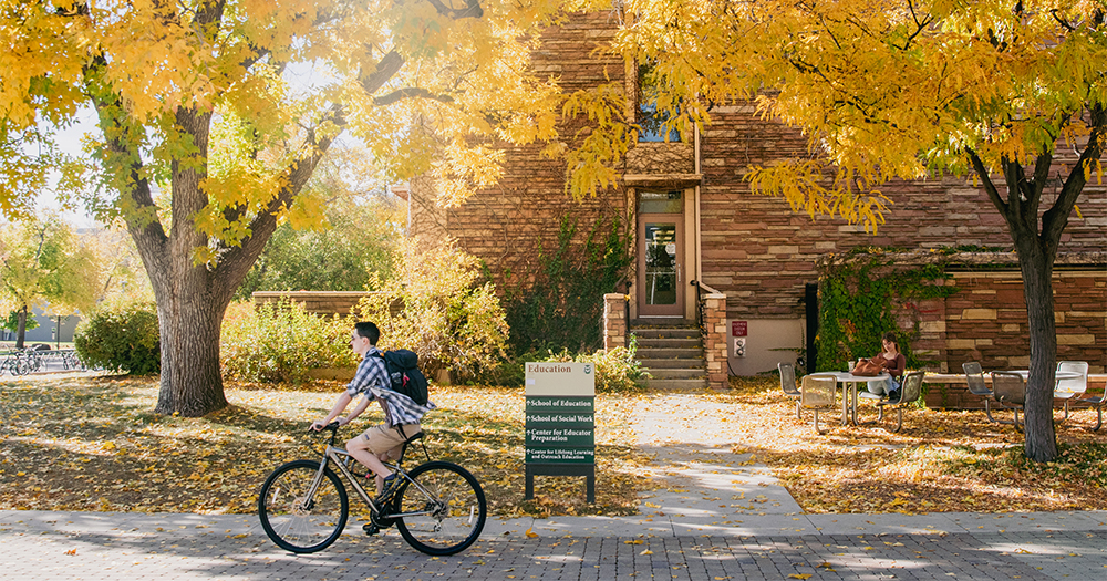 Person riding bike past CSU building and trees with golden leaves