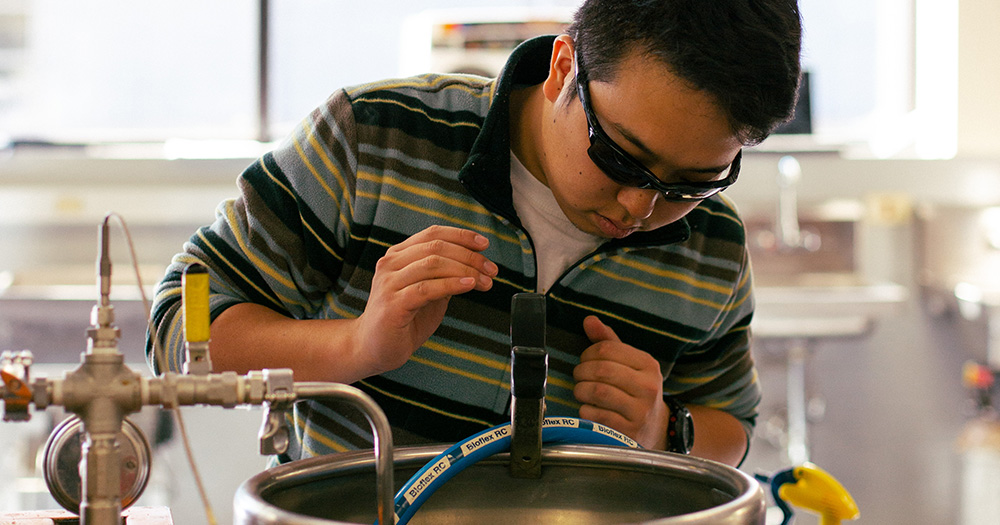A fermentation student works with a fermenting device in a lab