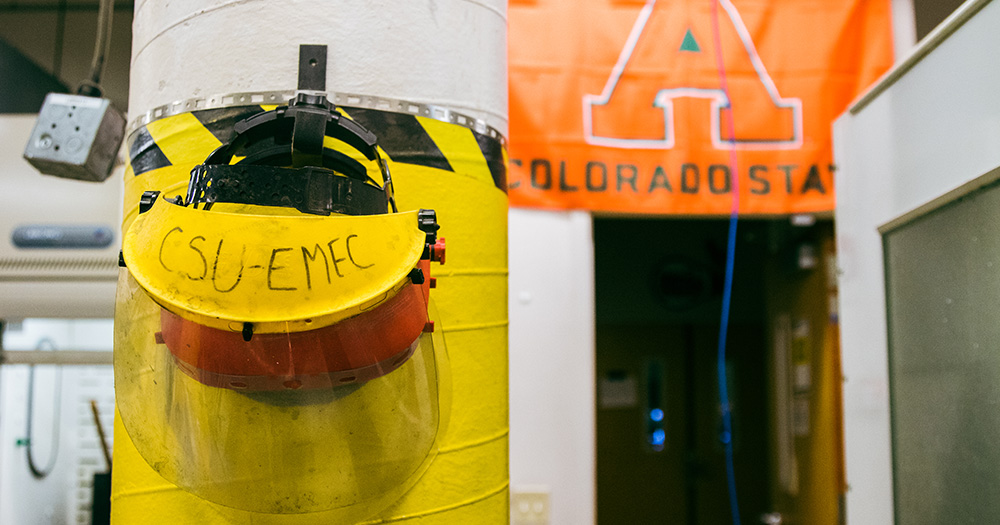 A safety hat hangs in the EMEC lab. In the distance a CSU aggies flag hangs.