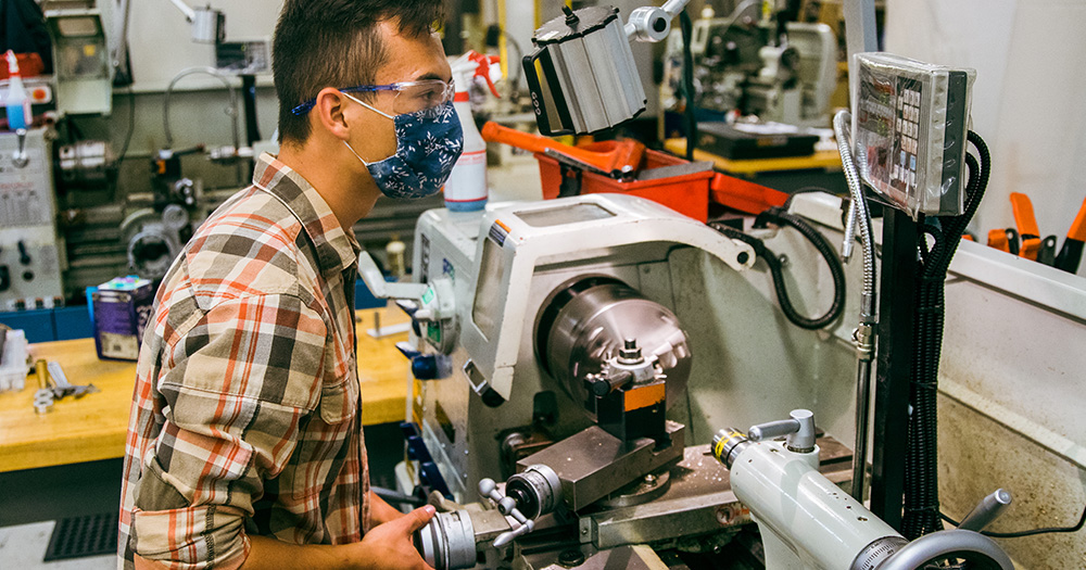 an engineering student works on a sophisticated metal mill, shaving metal into a screw or drill bit