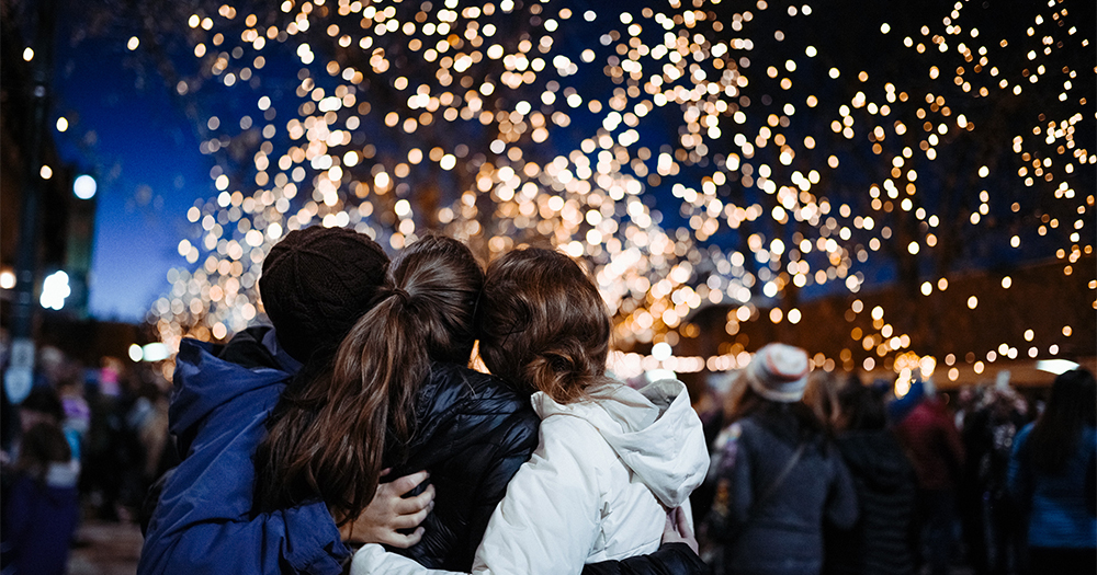 Three friends embrace while gazing at the beauty of hundreds of holiday lights sparking around Old Town, Fort Collins.
