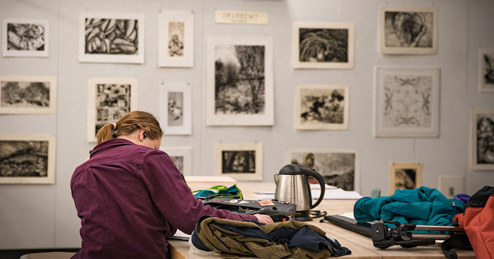 An art student sketches in front of a wall of artwork