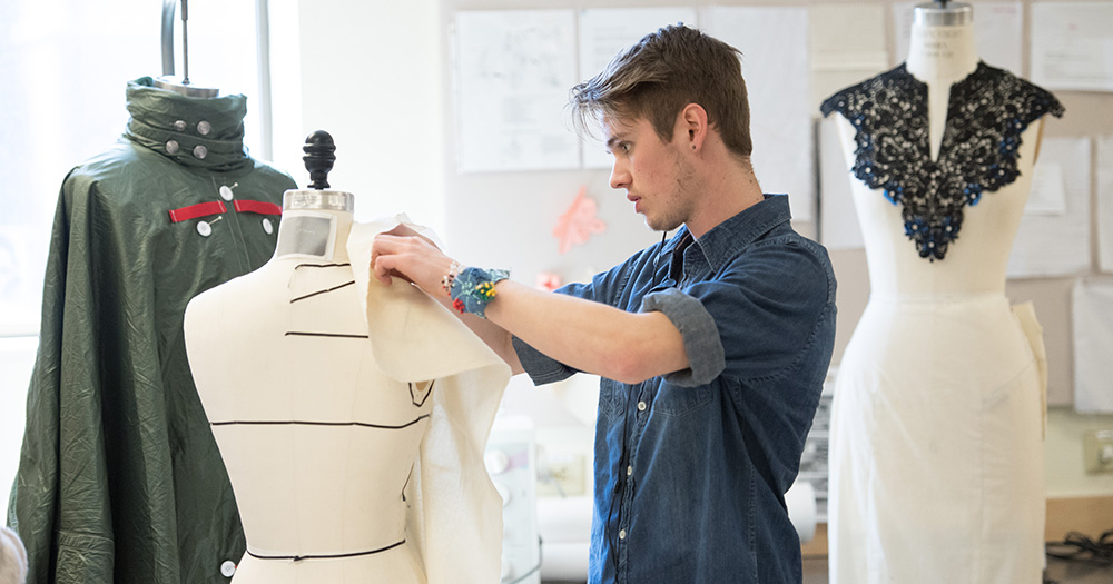 An apparel student pins fabric on a costume figure before a fashion show