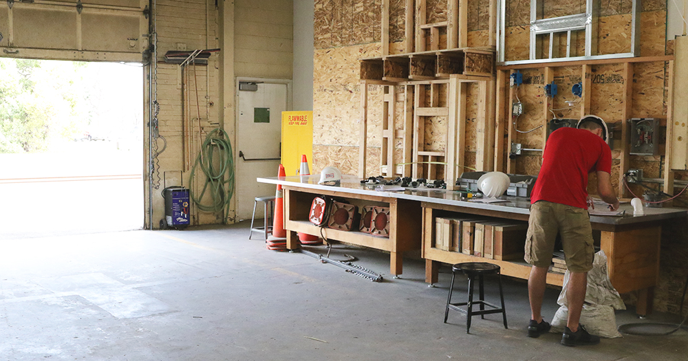 A garage door is open wide to a construction lab, which features tools, workbenches, and safety materials