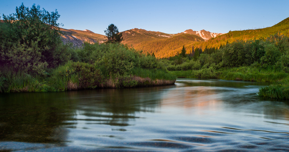 A shot of the rocky mountains in the distance with a clear, flowing creek in the foreground