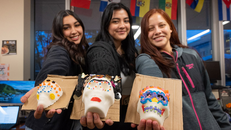 Students hold up sugar skulls they decorated with El Centro
