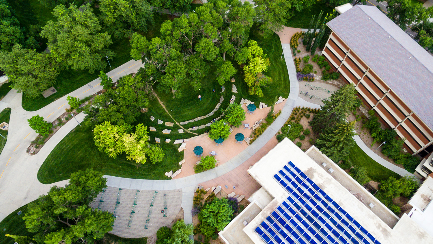 Aerial view of campus with lots of solar panels, trees, grass, and bike racks below