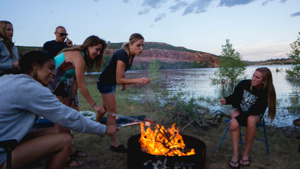 Students roast marshmallows over campfire with Horsetooth Reservoir in background