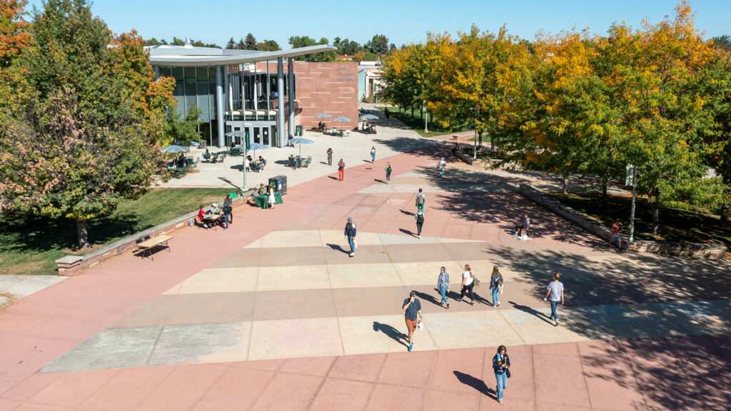 Students walk and skateboard across a wide plaza in early fall
