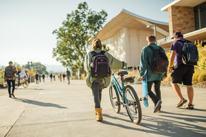 Students walking with bike and skateboard.