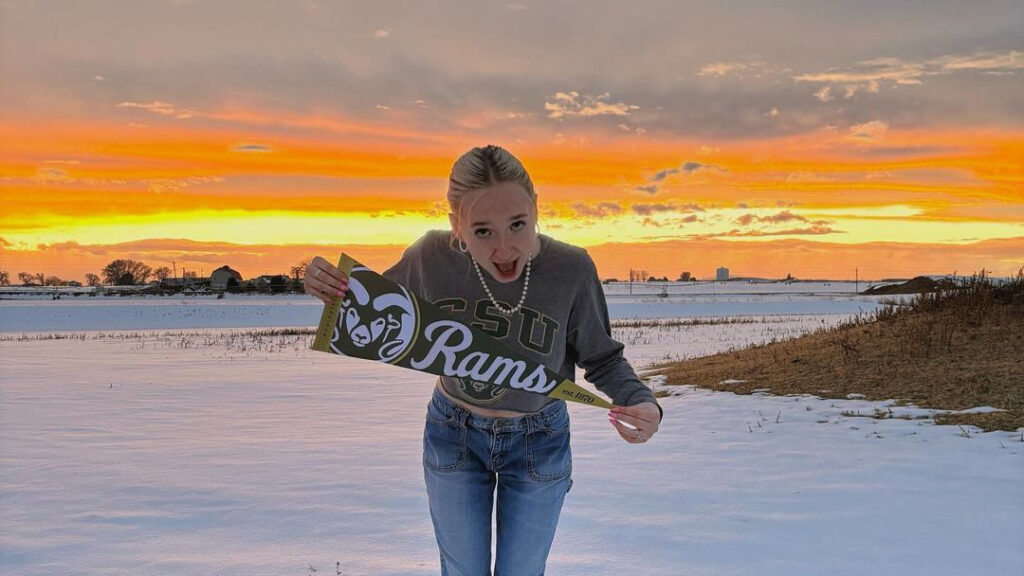 Woman holding Rams banner with excited look on her face outside at sunset in the snow